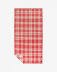 The Slowtide Palaka Woven Beach Towel in Guava, featuring a red and white plaid pattern, is laid flat on a white background with one corner folded to reveal the reverse side.