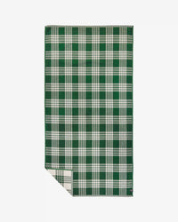 The Slowtide Palaka Woven Beach Towel in Sequoia, featuring a green and white checkered design, is laid flat on a white surface with one corner gently folded over.