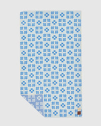 The Dream Oversized Premium Woven Towel in Lagoon by Slowtide features a blue geometric pattern on white plush cotton, with a small brown patch in the bottom right corner.
