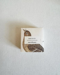 A small box of Bird Bath - Handmade Soap by The Quiet Botanist, featuring a bird illustration and label, rests on a light textured surface.