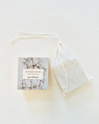 A small box labeled Mother Nature - Handmade Soap by The Quiet Botanist sits next to a white drawstring pouch on a light surface, promising deep hydration with every use.