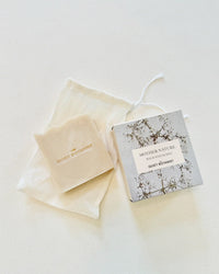 A bar of The Quiet Botanists Mother Nature - Handmade Soap rests on a cloth pouch beside its botanical-themed box, offering gentle cleansing and deep hydration.