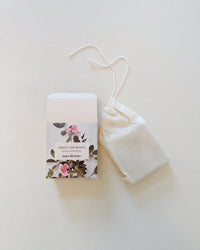 A white rectangular box with a floral design and Smell The Roses - Handmade Soap by The Quiet Botanist sits beside a small white drawstring pouch on a light surface.