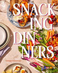 A vibrant table with fresh veggies, dips, fruits, bread, and cheese sits under bold white and pink text: Snacking Dinners by Chronicle Books—cookbook author Georgia Freedman’s name highlighted in orange for self-care meals.
