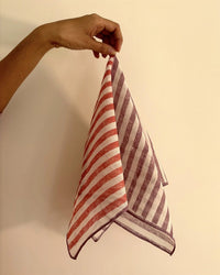 A hand displays the Casa Amarosa Stripe Hand Block Printed Scarf in Purple & Red, featuring diagonal stripes on a plain beige background.