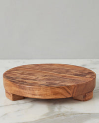 The etúHOME New Classic Round Trivet Riser, Medium, crafted from reclaimed acacia wood with short block feet, stylishly elevates kitchen essentials atop a white marble surface set against a light gray background.
