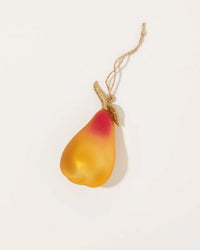 The Cody Foster Orchard Pear in Yellow + Gold is a pear-shaped glass ornament with a yellow-to-red gradient, glittery gold stem, and brown twine loop for hanging, displayed on a plain white background.