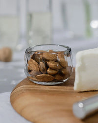One of The Collectives Pebbled Condiment Bowls (set of 4) holds whole almonds on a wooden board beside a block of white cheese and a cheese knife.