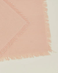 A close-up of two overlapping Hawkins New York Essential Cocktail Napkins in Blush, made from 100% cotton with frayed edges, arranged on a light surface.