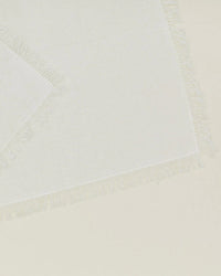 A close-up of Hawkins New York Essential Cocktail Napkins in Ivory (Set of 4) shows their textured 100% cotton fabric and delicate, uneven fringe edges, beautifully layered on a matching surface.