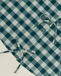 Close-up of the Hawkins New York Essential Gingham Tree Skirt in Sky/Peacock, featuring a blue and white checkered pattern with two tied fabric bows on top.