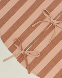 Close-up of the Hawkins New York Essential Striped Tree Skirt in Blush/Terracotta, featuring alternating stripes and two fabric ties in bow shapes near the center and right side.