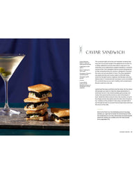 A martini glass with an olive stands next to a stack of neatly layered caviar sandwiches from Snacking Dinners by Chronicle Books, arranged on toasted bread against a dark surface with a blue background.
