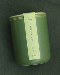 The LEIF Fern & Eucalyptus Candle is a 4 oz green jar with a matching lid and vertical label, filled with a soothing soy wax blend and set against a dark green background.
