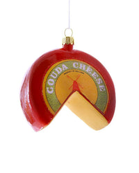 The Cody Foster Gouda Cheese Wheel Ornament is a hand-crafted Christmas decoration shaped like a red wax-covered wheel of Gouda cheese with a wedge cut out, revealing yellow cheese inside. It comes with a hanging loop on top.