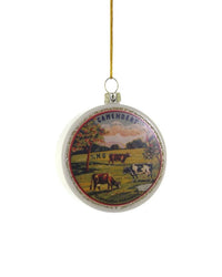 The Cody Foster Camembert Ornament is a round glass piece with a vintage cheese label design, showing cows in a scenic field. It hangs by a gold string—perfect for adding charm to your handcrafted decoration collection.