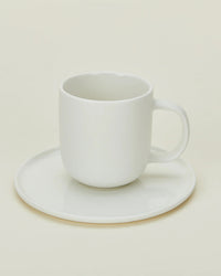 The Hawkins New York Simple Porcelain Espresso Cups & Saucers - Set of 2 features elegant white cups on matching saucers, pictured against a soft, neutral background.