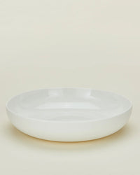 A set of 4 Simple Porcelain Low Bowls by Hawkins New York, featuring a plain, round white design with a subtly raised edge, displayed on a light cream background.