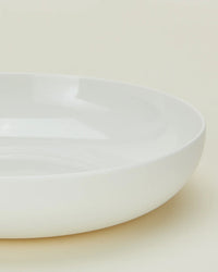 A close-up of a Simple Porcelain Low Bowl from Hawkins New York, part of a set of 4, shown from the side against a neutral background, highlighting its smooth surface and gently raised rim.