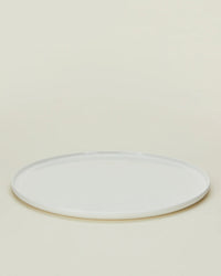 A Simple Porcelain Salad Plate from Hawkins New Yorks set of 4 is displayed empty on a light beige background, viewed from a slight angle. The plain, round white plate evokes fine dinnerware style.