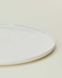 A close-up of the Hawkins New York Simple Porcelain Salad Plates (Set of 4) shows a portion of one sleek, round plate against a light beige background.