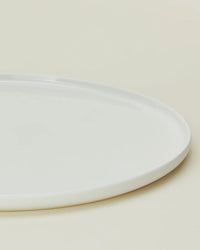 A close-up of a Hawkins New York Simple Porcelain Dinner Plate from the Set of 4, partially visible on a light beige surface.