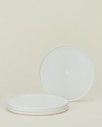 A set of four Simple Porcelain Salad Plates by Hawkins New York is stacked, with one plate upright behind the stack, shown against a neutral light background.