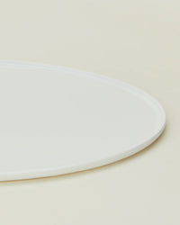 Close-up of the Hawkins New York Simple Porcelain Serving Platter—partially visible—showcasing its clean, white design against a light beige background.