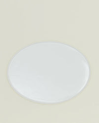 The Simple Porcelain Serving Platter by Hawkins New York, an oval white dish with a glossy finish, sits centered on a light beige background, showcasing the refined elegance of porcelain dinnerware.