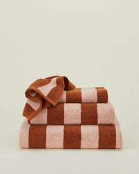 A neatly folded stack of Hawkins New York Simple Striped Terry Bath Sheets in Blush/Terracotta sits against a plain, light background.