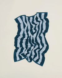 A Simple Striped Terry Washcloth in Sky/Peacock by Hawkins New York, featuring alternating dark and light blue vertical stripes, is crumpled on a plain, light-colored surface.