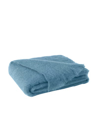 The Brushed Mohair Throw in Denim by Lands Downunder is a soft, fuzzy blue accent piece, shown folded against a plain white background. Woven in New Zealand, this luxury throw features a plush mohair texture.