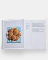 An open copy of The Spanish Mediterranean Islands Cookbook by Phaidon Press shows a photo of eight round buns on a plate atop a blue cloth and a recipe page titled Anytime Buns featuring Mediterranean instructions and ingredients.