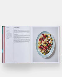 An open copy of *The Spanish Mediterranean Islands Cookbook* by Phaidon Press shows a Farmer’s Salad recipe and a photo of the finished dish with pasta, eggs, tomatoes, and greens, celebrating classic Mediterranean flavors.