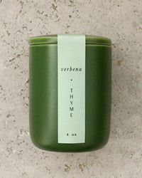 A green ceramic jar labeled Verbena & Thyme 4 oz by LEIF features a soy wax blend and wooden wick, set on a speckled stone surface.