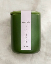 The LEIF Watermint & Clover Candle is a green 4 oz reusable ceramic jar with a white label, made from a soy wax blend, and displayed on a lightly textured surface.