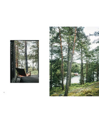 A cozy chair by a window in a forest cabin overlooks tall pines and a river; across the water, the Outdoor Chic by Cozy Publishing—a small red house—enhances the serene archipelago landscape.