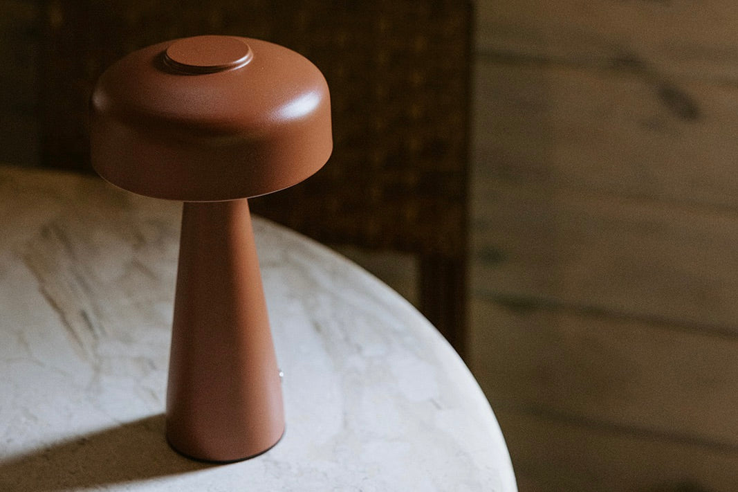 A modern, brown, mushroom-shaped table lamp sits on a round marble surface with a dark background.