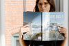 A woman with glasses holds and reads a book titled The Maine House II with a cover photo of a lighthouse and seagulls.