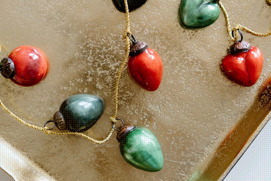 A garland of red and green ceramic holiday light ornaments is arranged on a gold textured surface.