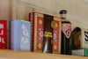 A shelf displays a Le Bon Garçon caramel box, a bottle labeled Ghia, and other colorful packaged items against a light wall.