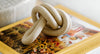 A speckled ceramic knot sculpture rests on a yellow book with floral imagery and the words DRIED FLOWER visible on the spine.