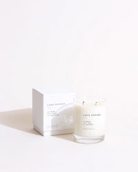 The Love Potion Classic 2-Wick Candle by Brooklyn Candle Studio, in a clear glass jar with minimalist black text, sits beside its matching white box against a plain light background.