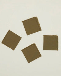 The Hawkins New York Essential Cocktail Napkins in Olive (set of 4), made from 100% cotton with frayed edges, are arranged diagonally on a plain light background.