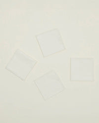 A set of four Essential Cocktail Napkins in Ivory by Hawkins New York, made from 100% cotton with fringed edges, are arranged in a loose, slightly tilted pattern on a plain light background.