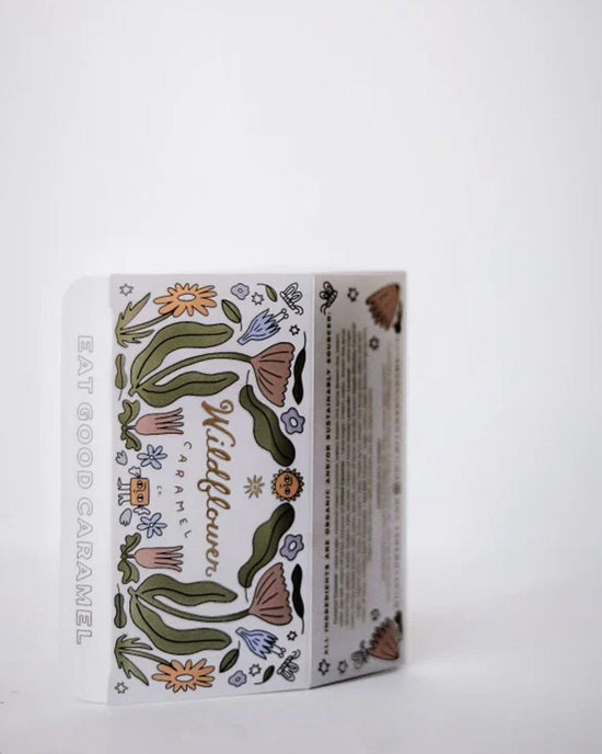 A rectangular Wildflower Caramel Co Assorted 6 piece box of Caramels features whimsical flower and green leaf drawings, "EAT GOOD CARAMEL" on the side, and is set against a plain white background.