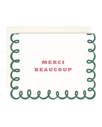 The Amy Heitman Merci Beaucoup | Single Card features green scalloped edges, "MERCI BEAUCOUP" in pink at the center, a blank interior, and comes with a matching envelope.