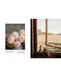 A photo from "Where Flowers Bloom" by Cozy Publishing features pink and white dahlias in a vase beside an open wooden window, with local cut flowers on the sill, overlooking a grassy field and trees.