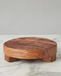 The etúHOME New Classic Round Trivet Riser, Small, is crafted from reclaimed acacia wood with short legs and sits elegantly on a white marble surface against a light gray background.