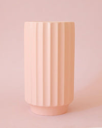 The Jungle Club Monroe Vase in Petal Pink, with a tall cylindrical shape and vertical ridges, is displayed against a matching petal pink background.